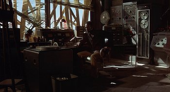 Movie still from “Vanishing Point” (1971), directed by Richard C. Sarafian – A man sitting in a chair in a room; Wide shot, Over the shoulder angle