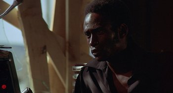 Movie still from “Vanishing Point” (1971), directed by Richard C. Sarafian – A man in a black shirt is sitting down; Close Up shot, Over the shoulder angle
