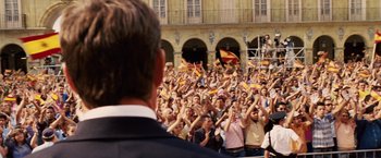 Movie still from “Vantage Point” (2008), directed by Pete Travis – A large crowd of people are gathered in front of a building; Wide shot, Over the shoulder angle