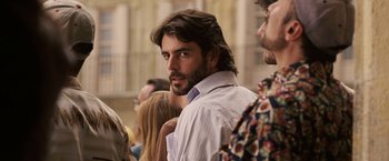 Movie still from “Vantage Point” (2008), directed by Pete Travis – A man with long hair and a beard is standing in a crowd of people; Close Up shot, Over the shoulder angle