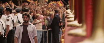 Movie still from “Vantage Point” (2008), directed by Pete Travis – A group of people standing in front of a crowd waving flags; Medium shot, Over the shoulder angle
