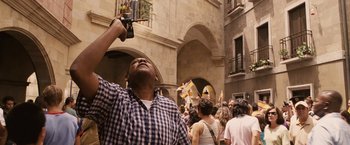 Movie still from “Vantage Point” (2008), directed by Pete Travis – A man holding a beer in a crowd of people; Medium shot, Low angle