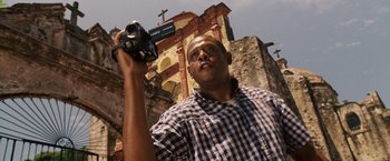 Movie still from “Vantage Point” (2008), directed by Pete Travis – A man is holding a video camera in front of a building; Close Up shot, Low angle