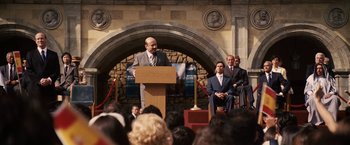 Movie still from “Vantage Point” (2008), directed by Pete Travis – A man in a gray suit is giving a speech; Wide shot, High angle