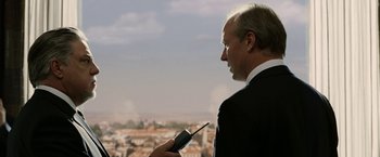 Movie still from “Vantage Point” (2008), directed by Pete Travis – A man in a black suit holding a cell phone; Medium shot, Over the shoulder angle