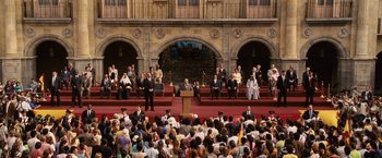 Movie still from “Vantage Point” (2008), directed by Pete Travis – A crowd of people sitting in front of a podium; Extreme Wide shot, High angle