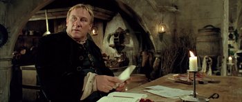 Movie still from “Vatel” (2000), directed by Roland Joffé – A man sitting at a table with papers in front of him; Medium shot, Low angle