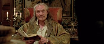 Movie still from “Vatel” (2000), directed by Roland Joffé – An older man sitting in a chair holding a book; Close Up shot, Low angle