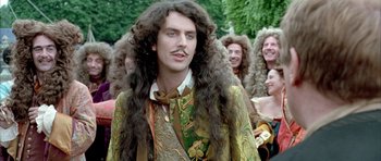 Movie still from “Vatel” (2000), directed by Roland Joffé – A man with long curly hair and a mustache standing in front of a group of people; Close Up shot, Over the shoulder angle