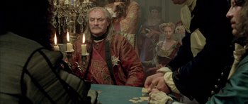 Movie still from “Vatel” (2000), directed by Roland Joffé – A man sitting at a table in front of a group of people; Medium shot, Over the shoulder angle