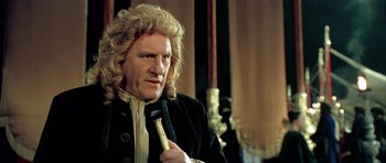 Movie still from “Vatel” (2000), directed by Roland Joffé – A man in a wig holding a microphone in his hand; Close Up shot, Low angle