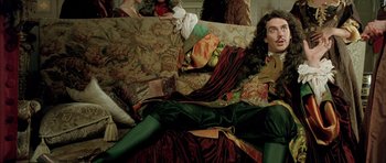 Movie still from “Vatel” (2000), directed by Roland Joffé – A man in a green suit is laying on a couch; Medium shot, Low angle
