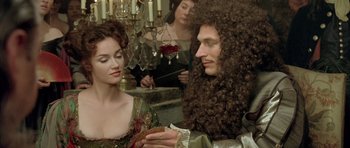 Movie still from “Vatel” (2000), directed by Roland Joffé – A man with a long curly hair is holding a cake; Medium shot, Over the shoulder angle