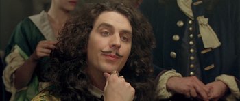 Movie still from “Vatel” (2000), directed by Roland Joffé – A man with long curly hair and a fake mustache; Close Up shot, Over the shoulder angle