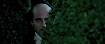 Movie still from “Vatel” (2000), directed by Roland Joffé – A man with a bald head is looking at the camera through a bush; Close Up shot, Over the shoulder angle