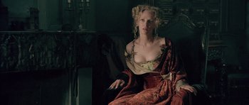 Movie still from “Vatel” (2000), directed by Roland Joffé – A woman sitting on a couch holding a remote control; Medium shot, Over the shoulder angle