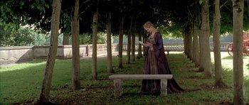 Movie still from “Vatel” (2000), directed by Roland Joffé – A woman dressed in medieval clothing standing next to a park bench; Wide shot, High angle
