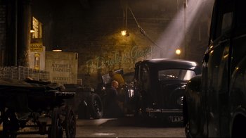 Movie still from “Vera Drake” (2004), directed by Mike Leigh – An old car is being worked on in a garage; Wide shot, Over the shoulder angle