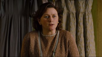 Movie still from “Vera Drake” (2004), directed by Mike Leigh – A woman in a brown dress is standing in front of a curtain; Medium shot, High angle