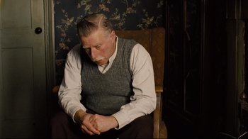 Movie still from “Vera Drake” (2004), directed by Mike Leigh – An older man sitting in a chair looking down; Medium shot, Low angle