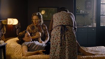 Movie still from “Vera Drake” (2004), directed by Mike Leigh – Two women and a man are sitting on a bed; Medium shot, High angle