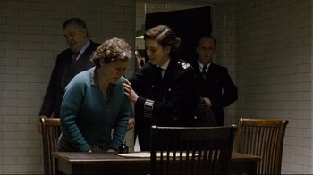 Movie still from “Vera Drake” (2004), directed by Mike Leigh – A group of people standing next to each other in a room; Medium shot, Over the shoulder angle
