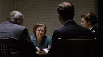 Movie still from “Vera Drake” (2004), directed by Mike Leigh – A woman sitting at a table in front of two men; Medium shot, Over the shoulder angle