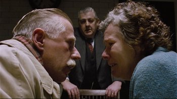 Movie still from “Vera Drake” (2004), directed by Mike Leigh – A man and a woman face each other in front of another man; Close Up shot, Over the shoulder angle