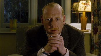 Movie still from “Vera Drake” (2004), directed by Mike Leigh – A man sitting down with his hands folded to his chest; Close Up shot, Low angle