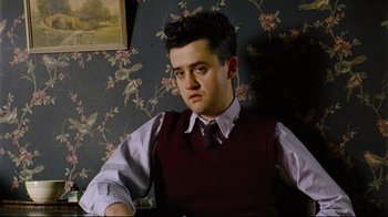 Movie still from “Vera Drake” (2004), directed by Mike Leigh – A man in a tie and vest sitting in front of a wall; Medium shot, Low angle