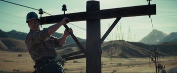 Movie still from “Vice” (2018), directed by Adam McKay – A man holding onto a wooden post with a power line in the background; Wide shot, Low angle