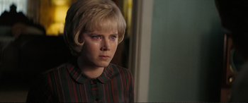 Movie still from “Vice” (2018), directed by Adam McKay – A young blonde haired woman wearing a striped shirt looking sad; Close Up shot, Over the shoulder angle