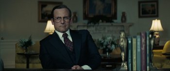 Movie still from “Vice” (2018), directed by Adam McKay – A man in a suit and tie sitting at a table; Close Up shot, Low angle
