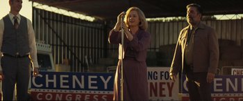 Movie still from “Vice” (2018), directed by Adam McKay – A woman in a purple dress holding a microphone; Medium shot, Low angle
