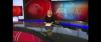 Movie still from “Vice” (2018), directed by Adam McKay – A woman sitting in front of a news desk; Wide shot, Low angle