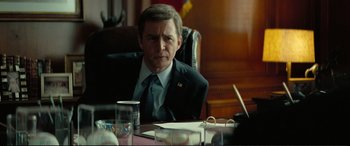 Movie still from “Vice” (2018), directed by Adam McKay – A man sitting at a table in front of papers; Medium shot, Over the shoulder angle