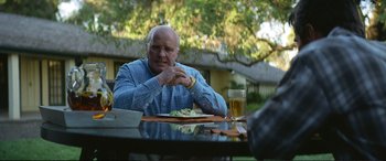Movie still from “Vice” (2018), directed by Adam McKay – An older man sitting at a table with a plate of food; Medium shot, Over the shoulder angle