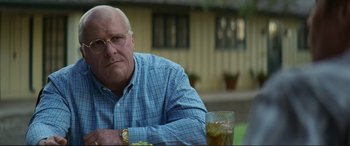 Movie still from “Vice” (2018), directed by Adam McKay – An older man sitting at a table with a glass of water; Close Up shot, Over the shoulder angle