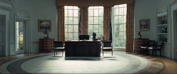 Movie still from “Vice” (2018), directed by Adam McKay – A desk and chairs in front of a large window; Wide shot, High angle