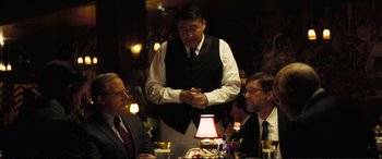 Movie still from “Vice” (2018), directed by Adam McKay – A man standing at a table with two other men; Medium shot, Over the shoulder angle