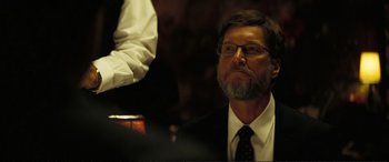 Movie still from “Vice” (2018), directed by Adam McKay – A man in a suit and tie sitting in front of a microphone; Close Up shot, Over the shoulder angle