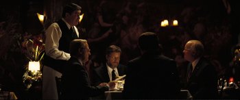 Movie still from “Vice” (2018), directed by Adam McKay – A group of men sitting at a table in front of a crowd; Medium shot, Over the shoulder angle