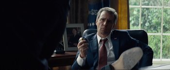 Movie still from “Vice” (2018), directed by Adam McKay – A man in a suit and tie holding an object in his hand; Close Up shot, Over the shoulder angle