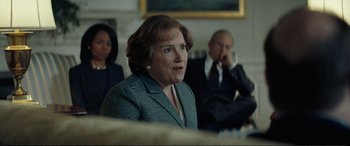 Movie still from “Vice” (2018), directed by Adam McKay – A woman in a green jacket is sitting in front of a group of people; Medium shot, Over the shoulder angle