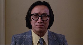 Movie still from “Videodrome” (1983), directed by David Cronenberg – A man with long hair and glasses wearing a suit and tie; Close Up shot, Low angle