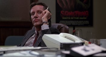 Movie still from “Videodrome” (1983), directed by David Cronenberg – A man sitting at a desk in front of a phone; Close Up shot, Low angle