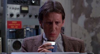 Movie still from “Videodrome” (1983), directed by David Cronenberg – A man holding a coffee cup while sitting in front of a computer; Close Up shot, Low angle