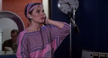 Movie still from “Videodrome” (1983), directed by David Cronenberg – A woman with a microphone in her hand; Medium shot, Over the shoulder angle