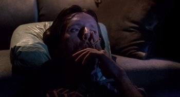 Movie still from “Videodrome” (1983), directed by David Cronenberg – A man sitting on a couch with a cigarette in his mouth; Close Up shot, Overhead angle