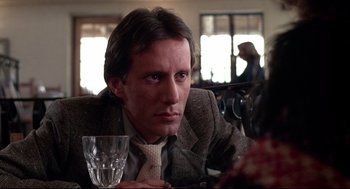 Movie still from “Videodrome” (1983), directed by David Cronenberg – A man sitting at a table with a glass of wine; Close Up shot, Low angle